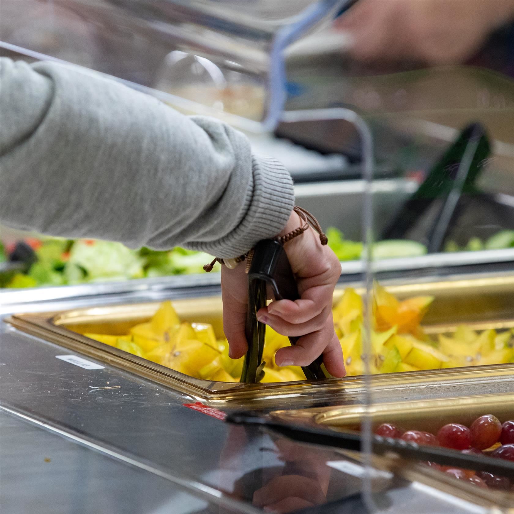  Student scoops fresh fruit and vegetables from lunch buffet